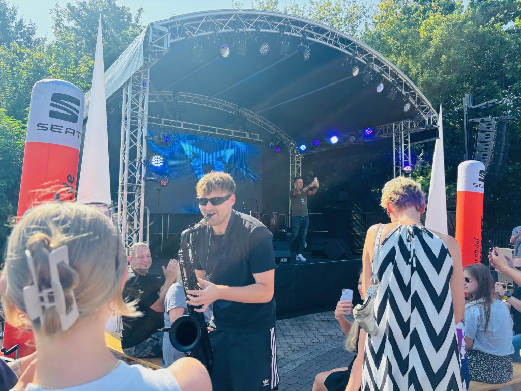 Es ist ein Saxophonist vor einer Bühne mit CUPRA Logo zu sehen. Um ihn herum stehen Besucher.
